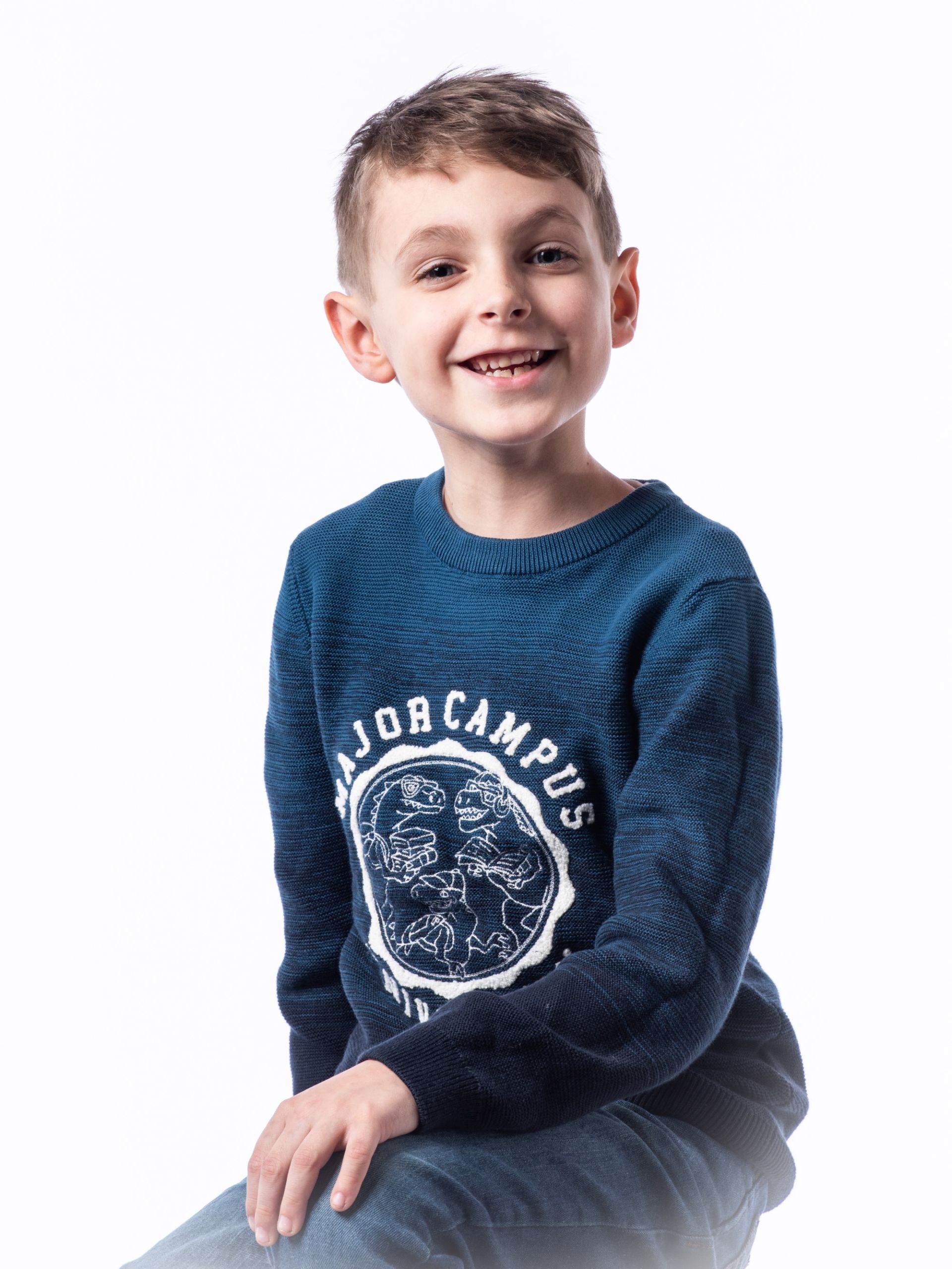 Portrait d'un enfant souriant en studio, vêtu d'un pull bleu.