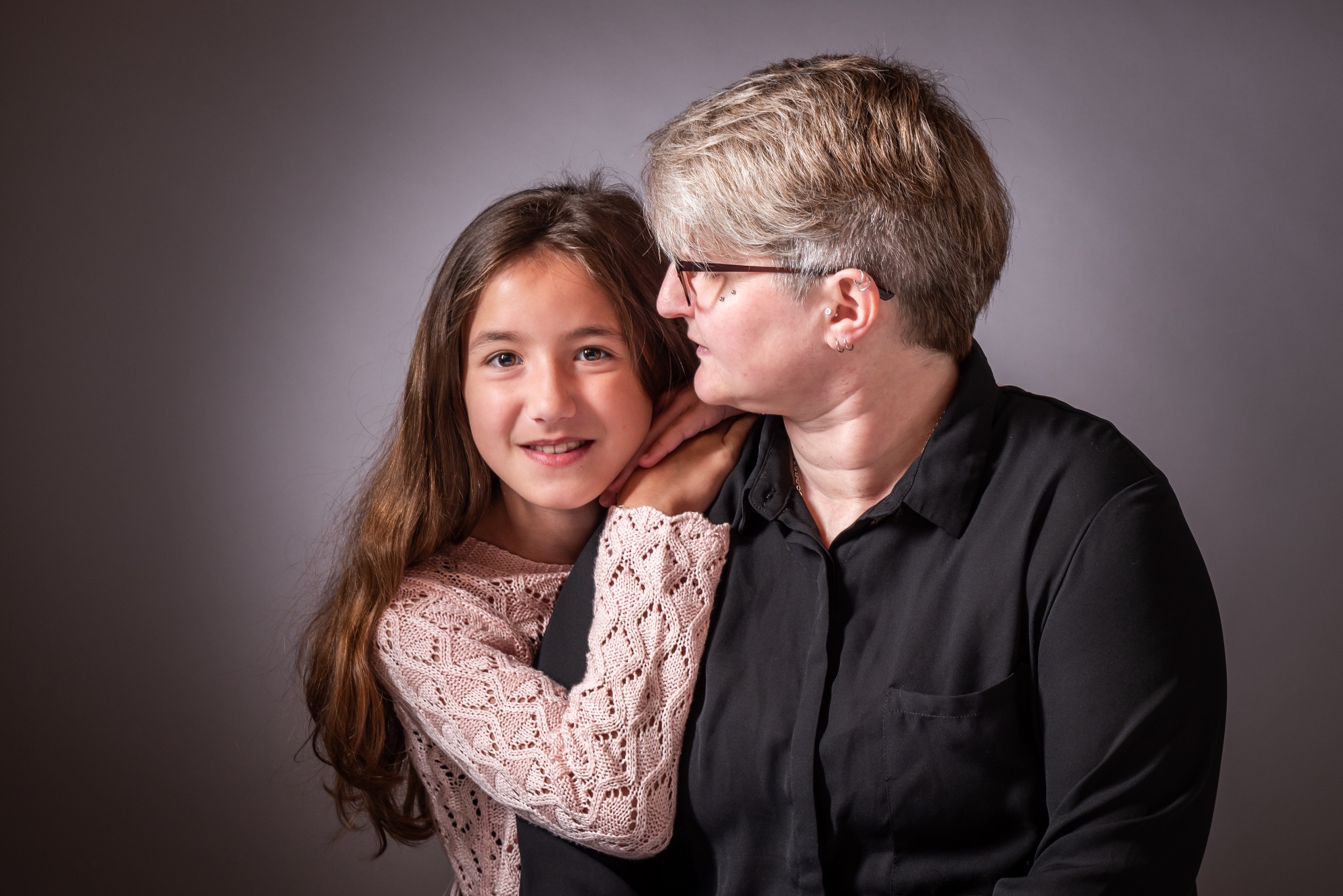 Portrait d'une mère et sa fille en studio, souriantes et complices.