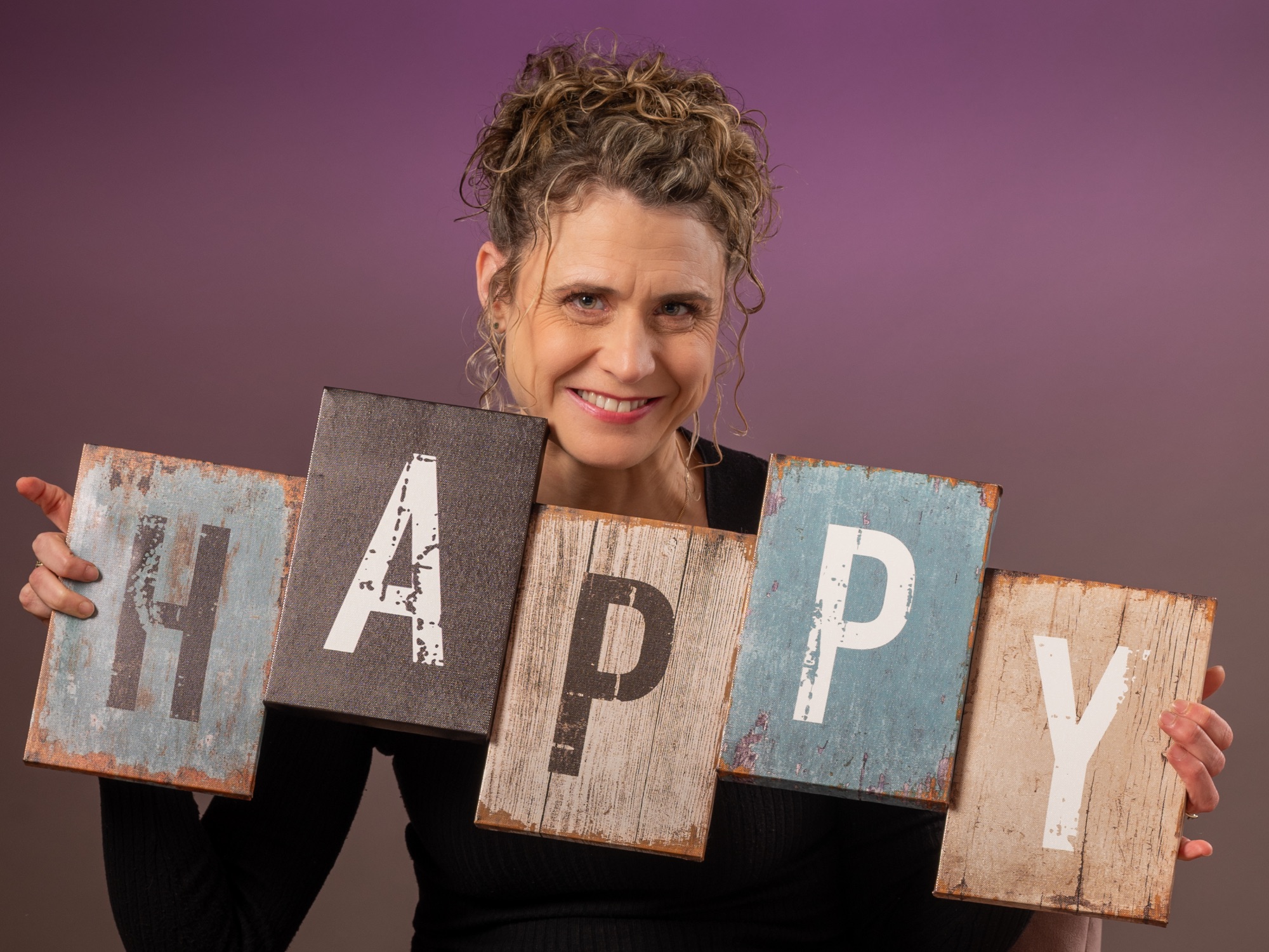 Portrait d'une femme souriante tenant des lettres formant le mot 'HAPPY'