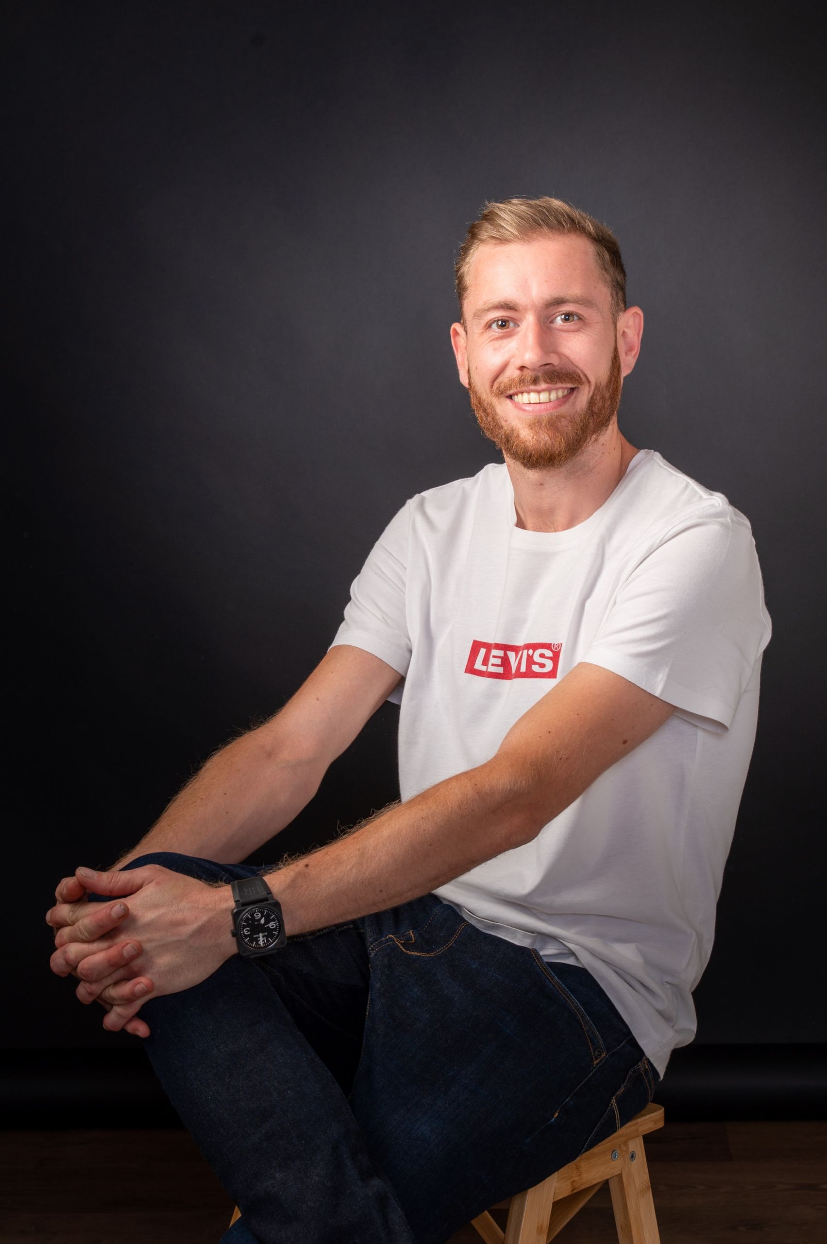 Portrait d'un homme souriant en studio, vêtu d'un t-shirt blanc.
