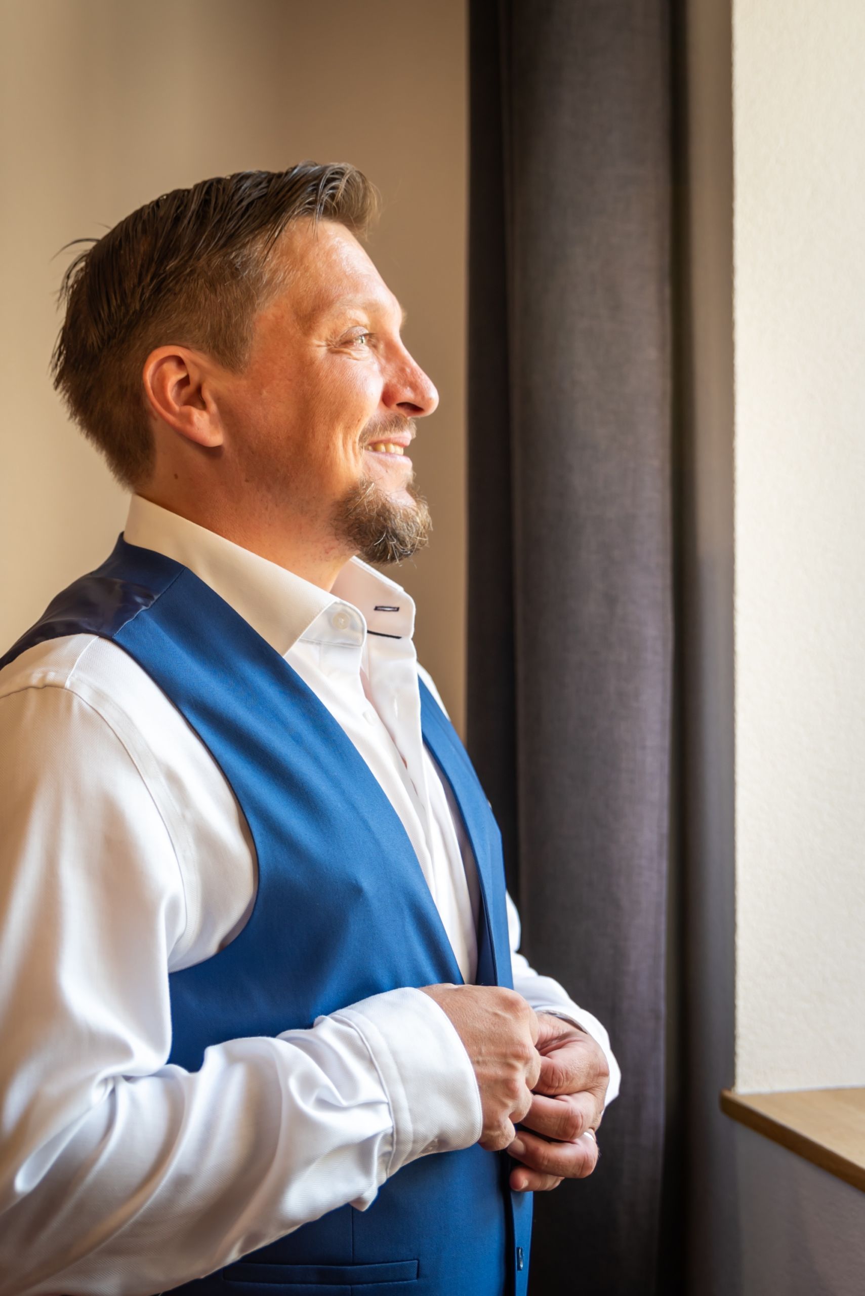 Homme en costume bleu se préparant pour un mariage, lumière naturelle.