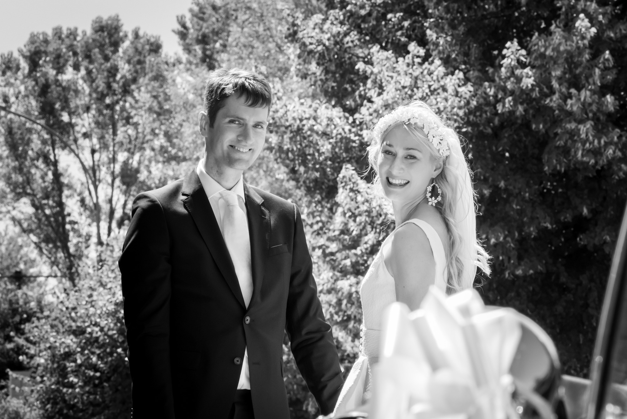 Couple de mariés souriant en extérieur, photo en noir et blanc.