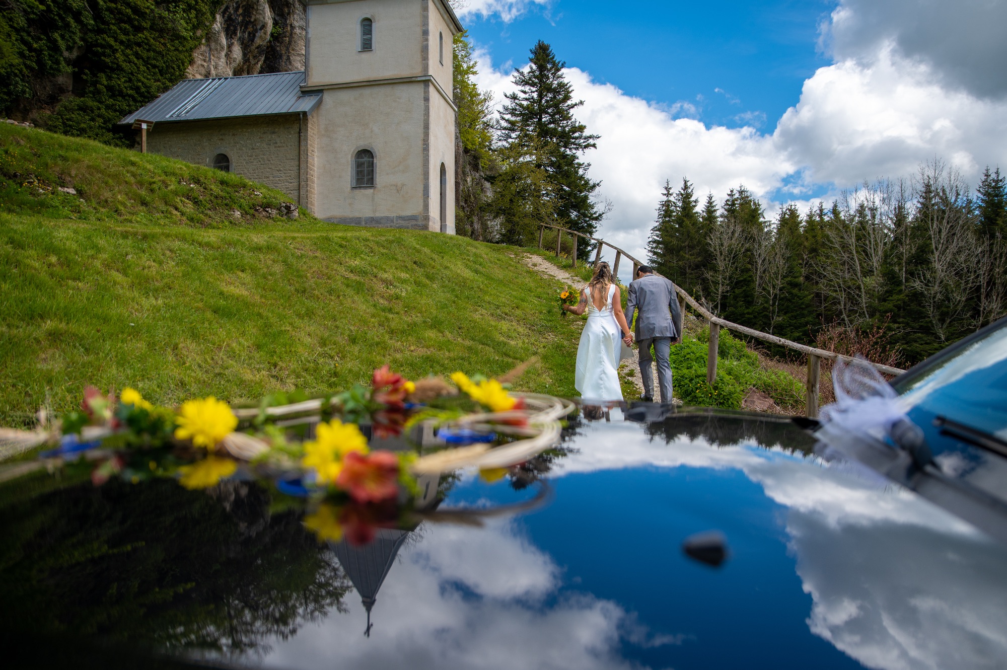 Couple de mariés marchant près d'un étang avec des fleurs.