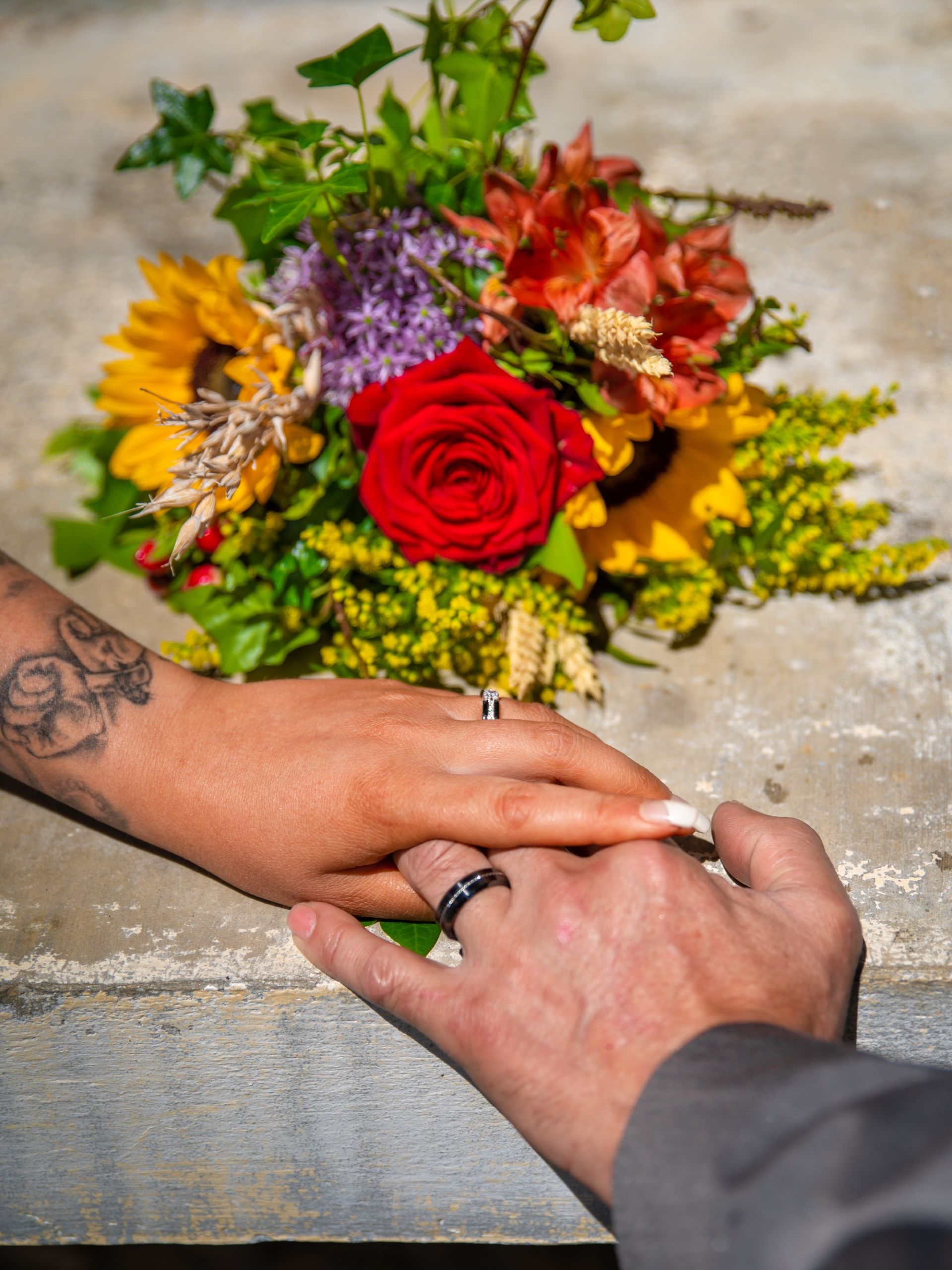 Mains entrelacées avec un bouquet de fleurs colorées lors d'un mariage.