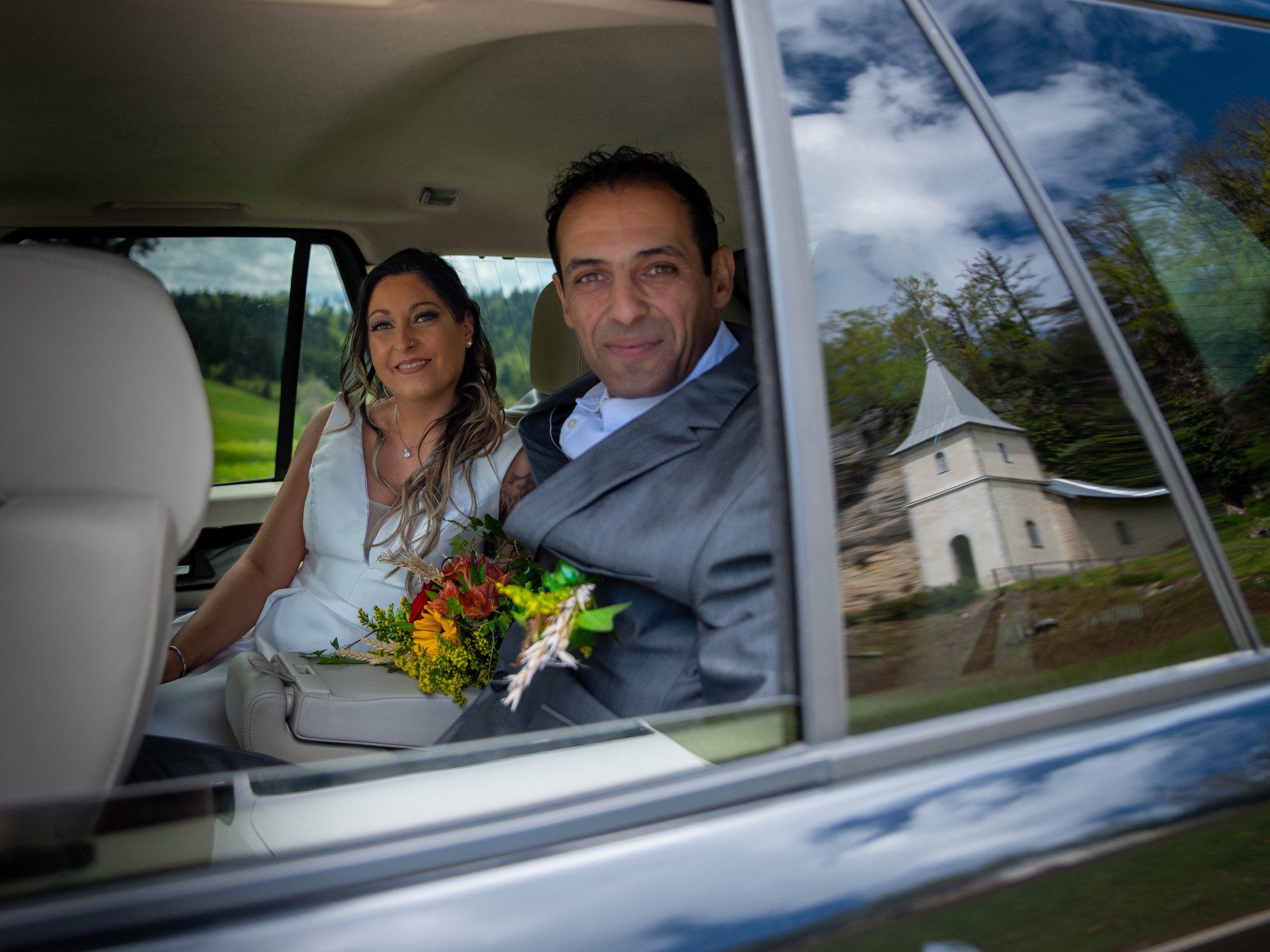 Couple de mariés dans une voiture, bouquet de fleurs à la main.