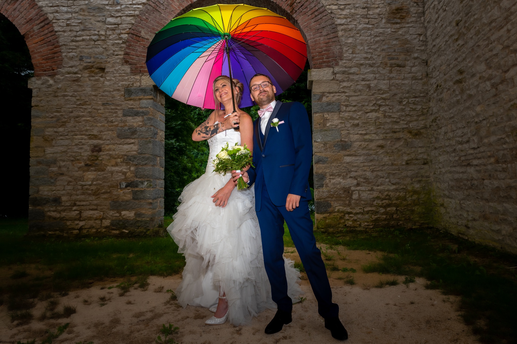 Couple de mariés sous un parapluie coloré, moment joyeux et authentique.